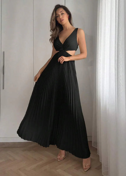Femme portant une robe longue plissée noire à décolleté, élégante, debout en intérieur lumineux.