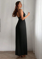 Femme portant une robe longue plissée noire élégante à bretelles, debout en intérieur