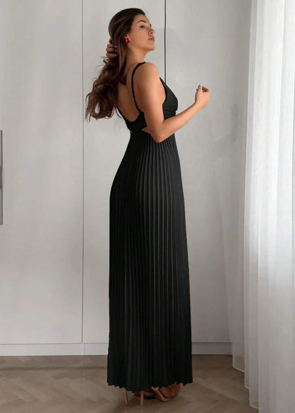 Femme portant une robe longue plissée noire élégante à bretelles, debout en intérieur