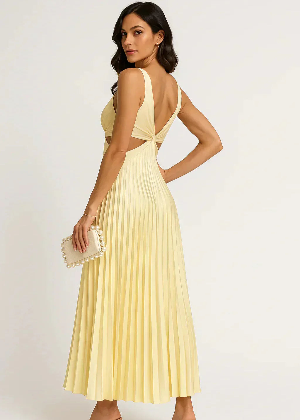 Femme portant une robe jaune plissée sans manches, détail dos nu, sac pochette perlé.