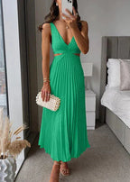 Femme en robe verte plissée élégante avec décolleté, sac à main perlé, debout en intérieur moderne