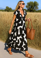 Femme en robe longue noire et blanche à motifs abstraits, sac marron, sandales d'été, champ