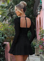 Femme de dos portant une robe noire à manches longues en dentelle, dos nu, en jardin fleuri.