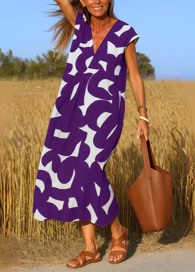Femme en robe longue violette à motif graphique, sandales et sac marron, champ de blé