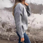 Femme portant un pull gris ample en maille et un jean, devant un mur texturé