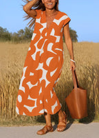 Femme en robe orange à motifs abstraits, sac marron, sandales, champ d'été en arrière-plan