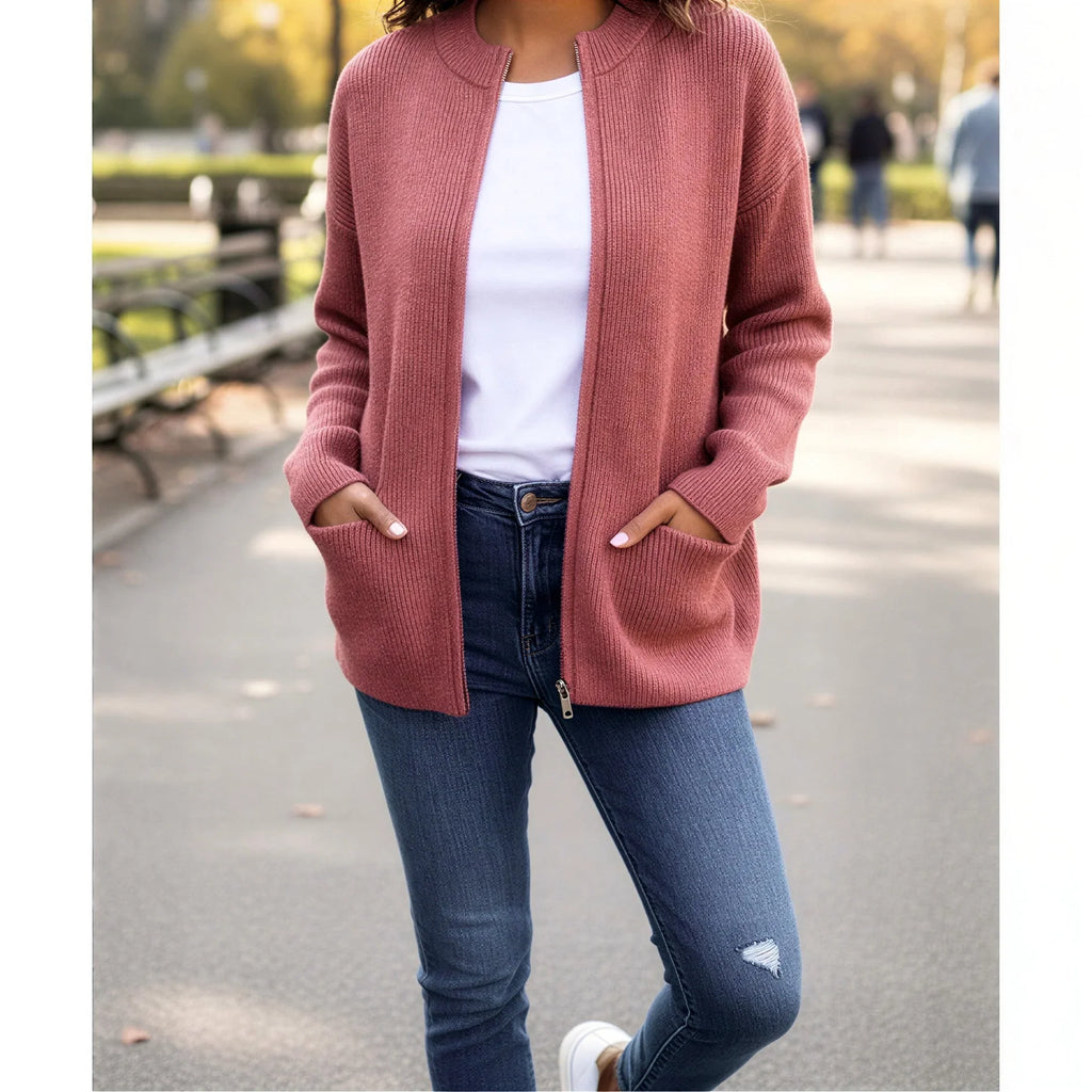 Femme portant un cardigan rose en maille, t-shirt blanc et jean, dans un parc urbain.