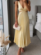 Robe longue plissée jaune pastel sans manches, décolleté, portée avec pochette perles, élégante.