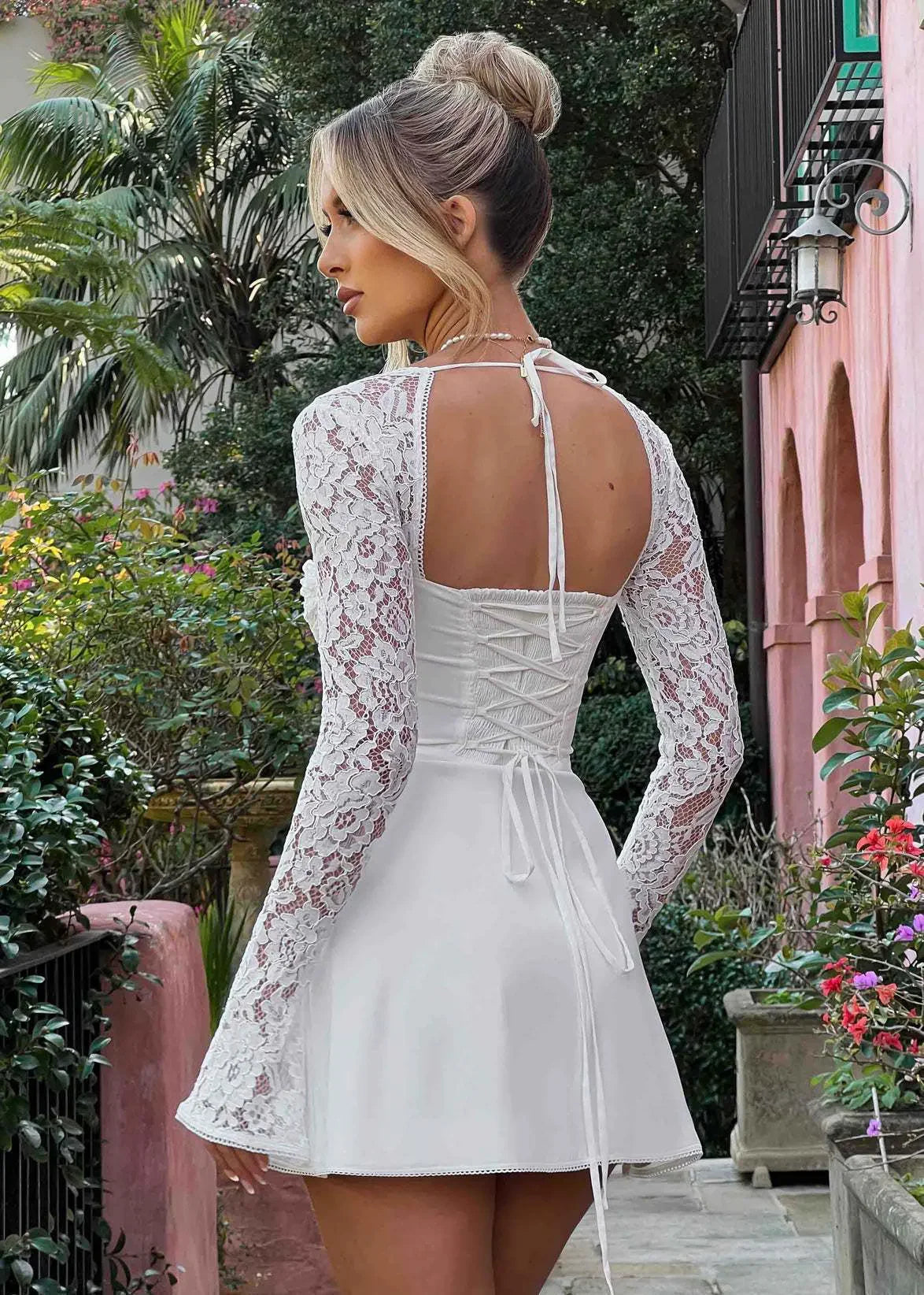 Robe blanche courte à manches longues en dentelle, dos lacé, femme dehors dans un jardin tropical.